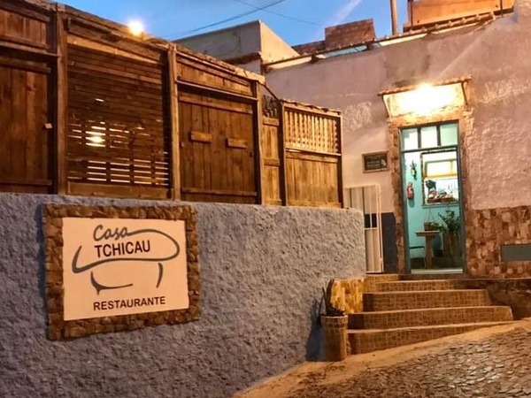 Exterior entrance of Casa Tchicau Restaurante with its wall sign and turquoise doorway.