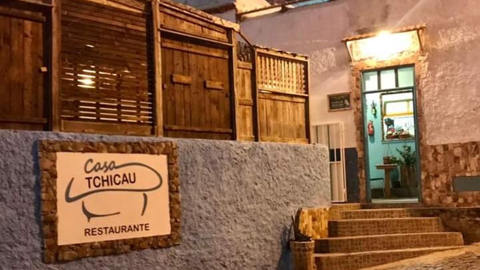 Exterior entrance of Casa Tchicau Restaurante with its wall sign and turquoise doorway.