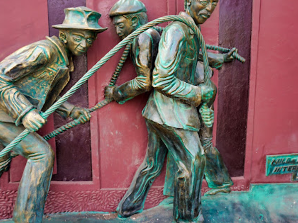 Bronze-colored sculpture of three figures pulling a rope, signed Nild-ro Interart 98.