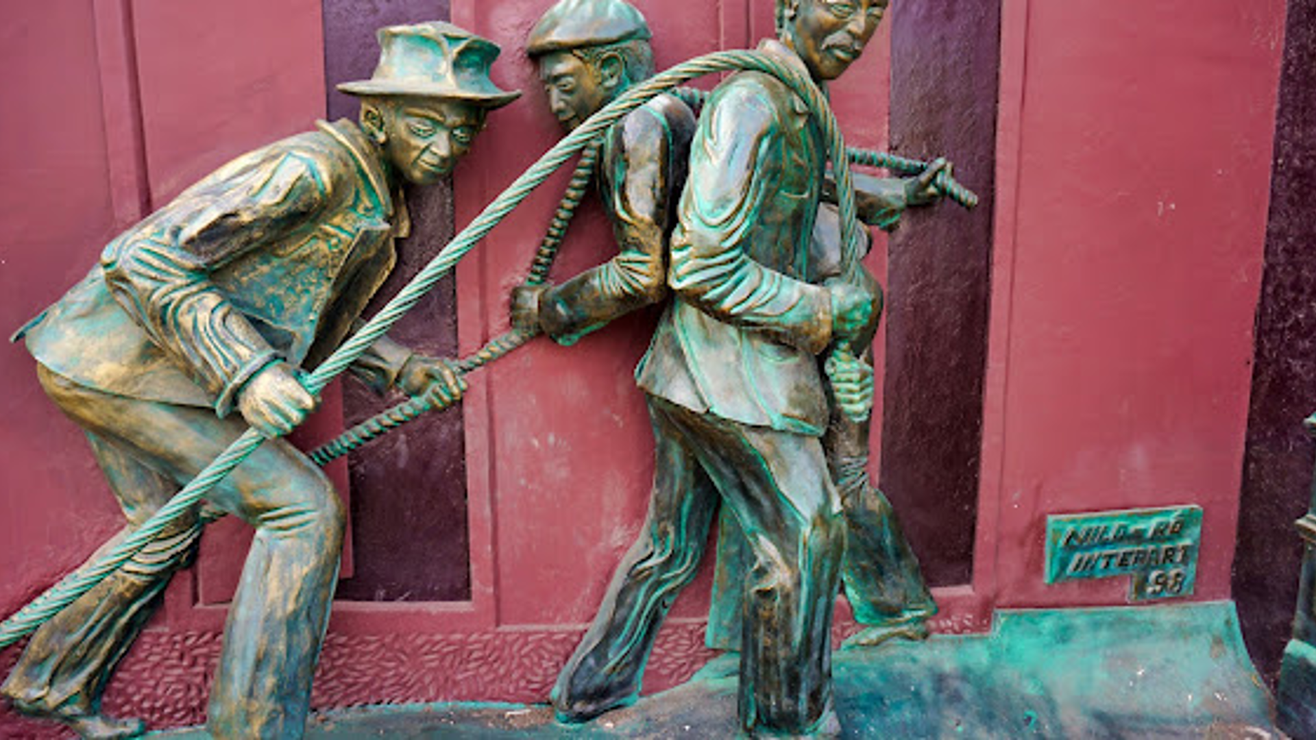 Bronze-colored sculpture of three figures pulling a rope, signed Nild-ro Interart 98.